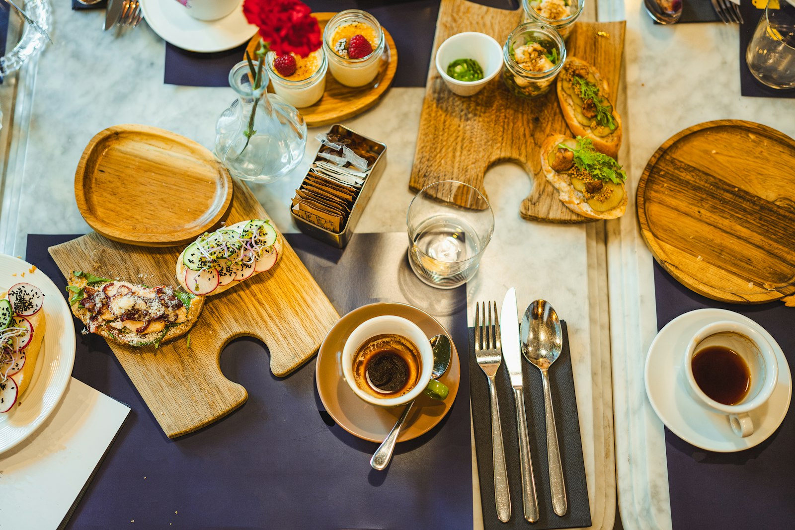 Frühstück von oben: belegte Brote auf Holzbrettern, Kaffee, Besteck und ein Glas Wasser.