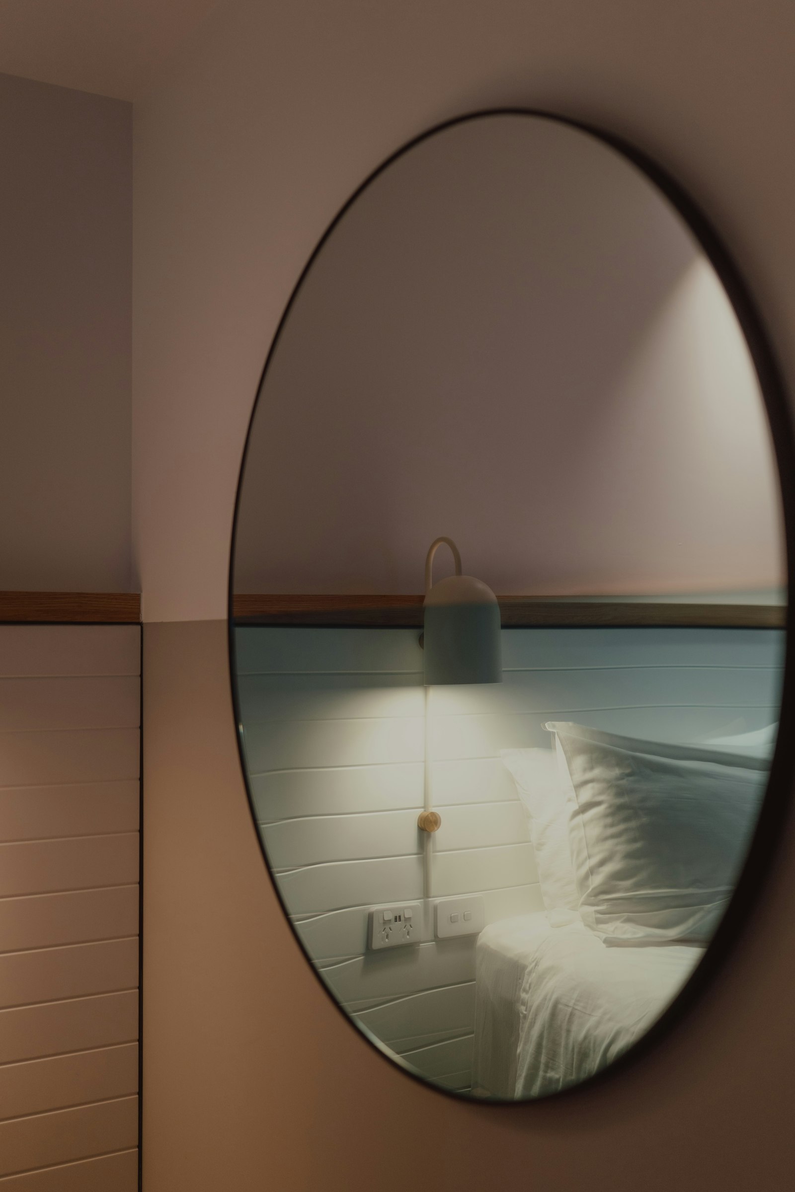 Blick durch einen runden Spiegel auf Bett und Leselampe.