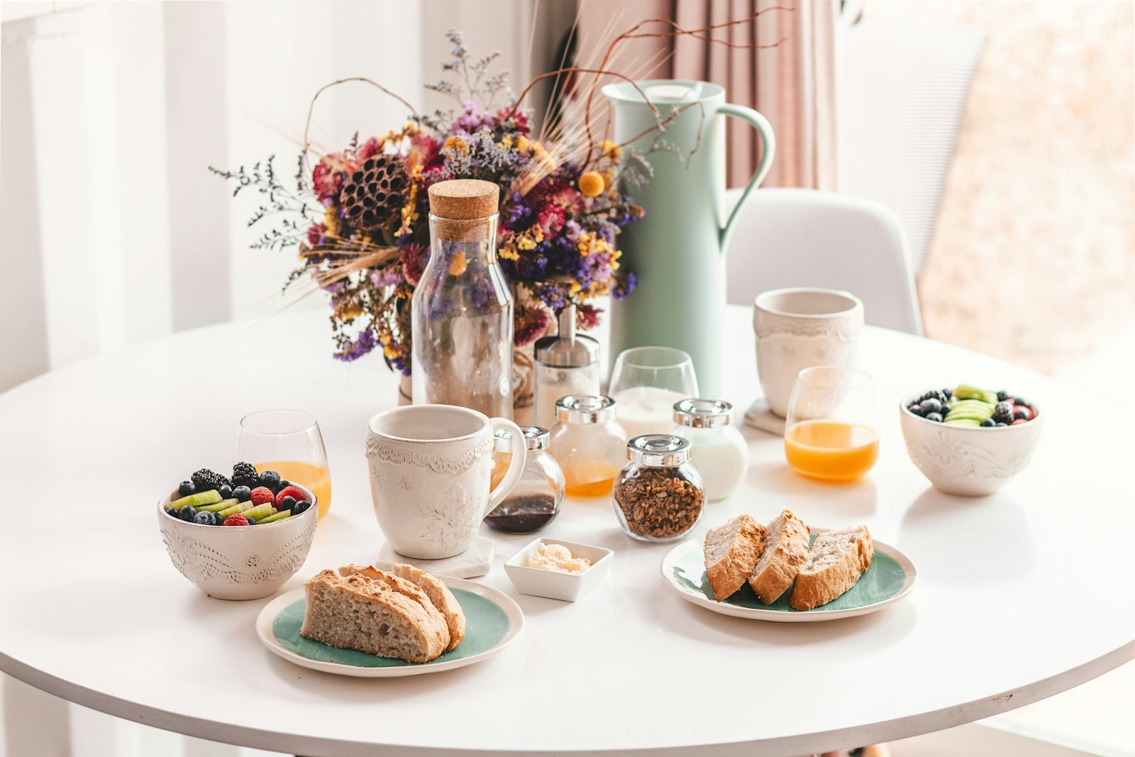 Gedeckter Frühstückstisch mit Gebäck, Obst, Joghurt und Saft.