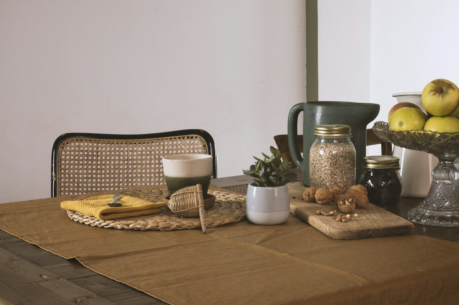 Holztisch mit Korb, Krug, Äpfeln und Gläsern.
